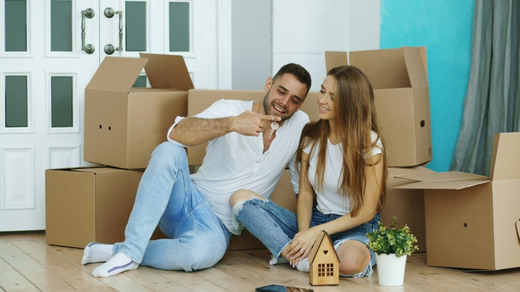 Young couple holding house keys on moving day surrounded by boxes in their new home