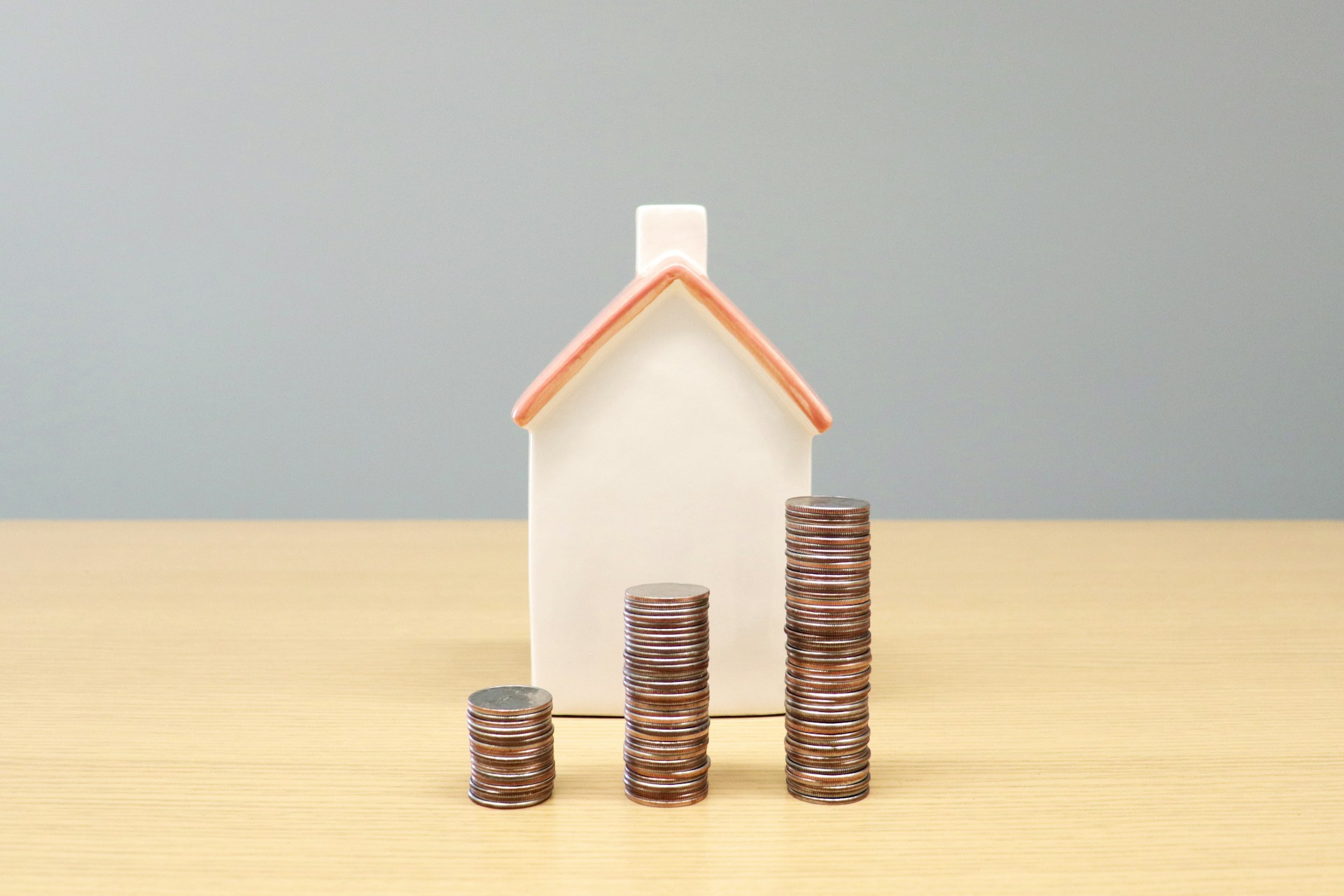 Small house model with growing coin stacks representing mortgage savings in Alberta