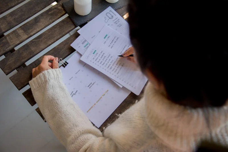 Person reviewing mortgage documents at a kitchen table with a laptop open, Calgary home interior visible