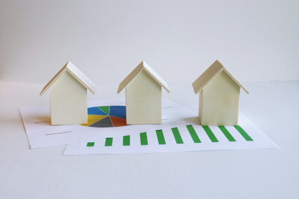 Three small wooden house models sitting on printed housing market charts and graphs