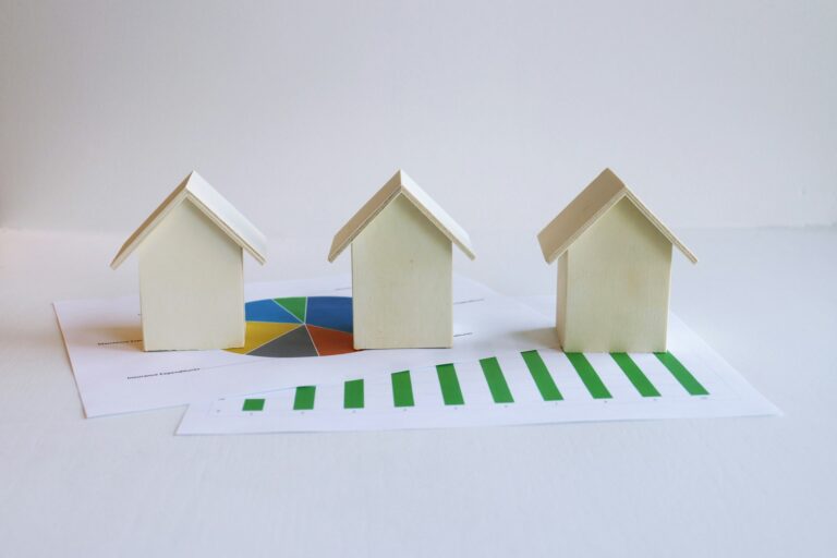 Three small wooden house models sitting on printed housing market charts and graphs