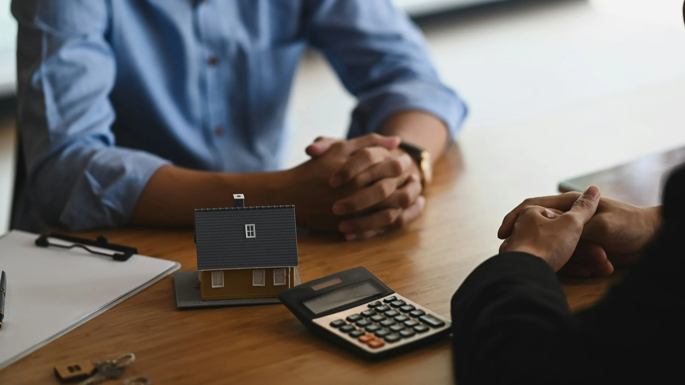 Mortgage affordability consultation with model house, calculator, and house keys on desk